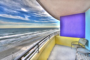 Uma varanda com vista para a praia e o oceano, uma cadeira e uma parede roxa.
