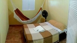 A small room with a bed, a hammock, a fan, and a window. - Casa na praia do preá (Cruz)