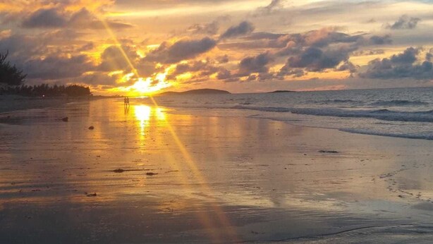 A beach scene with the sun setting over the horizon, casting a golden glow on the wet sand. - Casa na praia do preá (Cruz)
