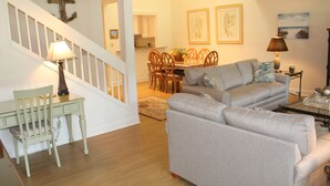Ein Wohnzimmer mit grauem Sofa, einem Holzesstisch mit Stühlen, einer Treppe mit weißer Geländer und einem Kreuz an der Wand.