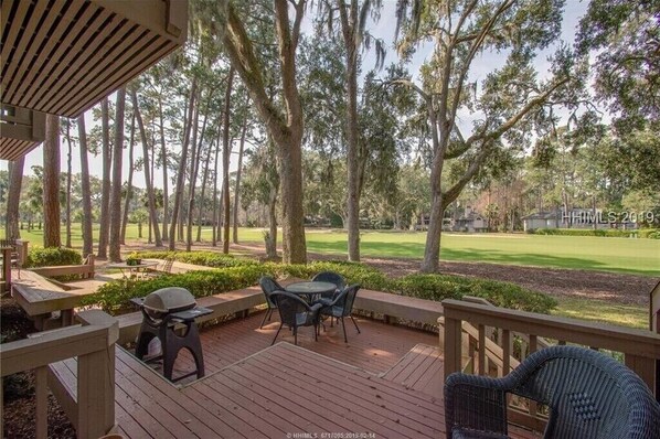A wooden deck with outdoor seating, overlooking a golf course.
