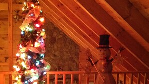 A cozy room with a wooden ceiling, a Christmas tree, a wicker chair, and a snowman decoration.