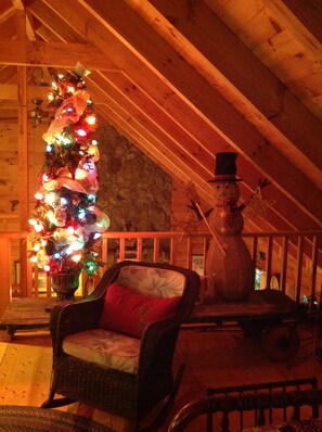 Una habitación acogedora con techo de madera, un árbol de Navidad, una silla de mimbre y una decoración de muñeco de nieve.