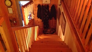 A wooden staircase with a railing, a coat rack with several coats, and a framed picture on the wall.
