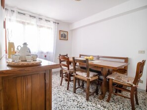 A dining area with a wooden table and chairs, a coffee set, and a window with curtains.
