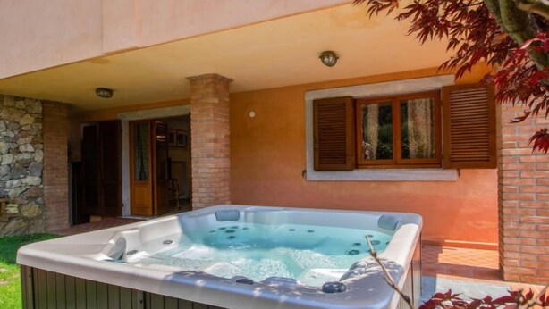 Un bain à remous situé dans un espace extérieur abrité, avec un mur en pierre et des volets en bois.