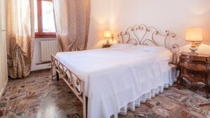 Une chambre à coucher avec un lit, deux tables de chevet, une fenêtre avec des rideaux et un radiateur.