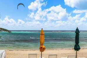 A beach with two umbrellas, a sandy shore, and a person kite surfing in the background. - Starfish at The Cottages | Breakfast Included (East End)