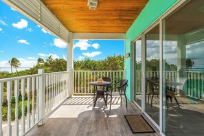 A covered balcony with a wooden ceiling, white railing, and a table with chairs.