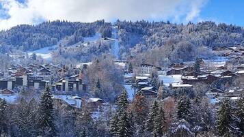 Un village de montagne enneigé, avec ses maisons traditionnelles en bois, une piste de ski et un ciel dégagé.