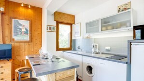 Une cuisine compacte agrémentée de touches de bois, un lave-linge et un coin repas avec des tabourets.