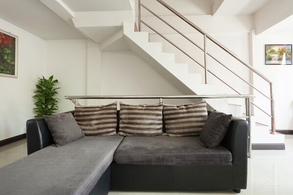 A modern living room with a black leather sofa, a striped throw pillow, a potted plant, and a staircase with a metal railing.