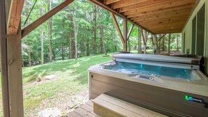 A hot tub with a control panel, surrounded by a wooden deck and a glass enclosure, overlooking a forested area. - Mountain Cabin with Access to Lakes & Waterfalls (Seven Devils)