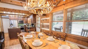 A wooden interior with a dining table set for four, a kitchen area, and large windows with blinds. - Mountain Cabin with Access to Lakes & Waterfalls (Seven Devils)