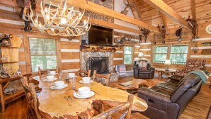 A rustic cabin interior with a dining area, fireplace, leather sofa, and various hunting trophies. - Mountain Cabin with Access to Lakes & Waterfalls (Seven Devils)