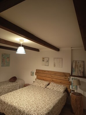 A bedroom with a sloped ceiling, wooden beams, two beds with patterned bedding, a hanging light fixture, and wall art.