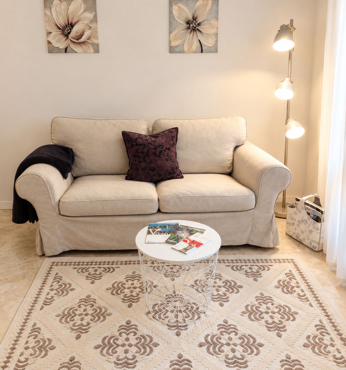 A living room with a beige sofa, a patterned rug, a small white table, and a floor lamp.