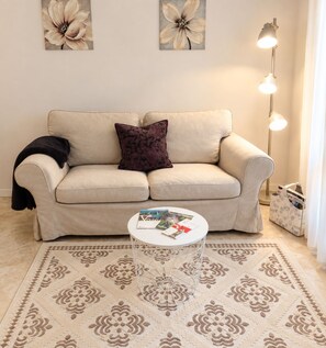 A living room with a beige sofa, a patterned rug, a small white table, and a floor lamp.