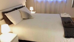 A neatly made bed with pillows, a bedside lamp, and a folded towel on the nightstand.