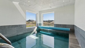 Una piscina interna moderna con pareti di vetro trasparenti, una panca blu e vista su un paesaggio erboso.