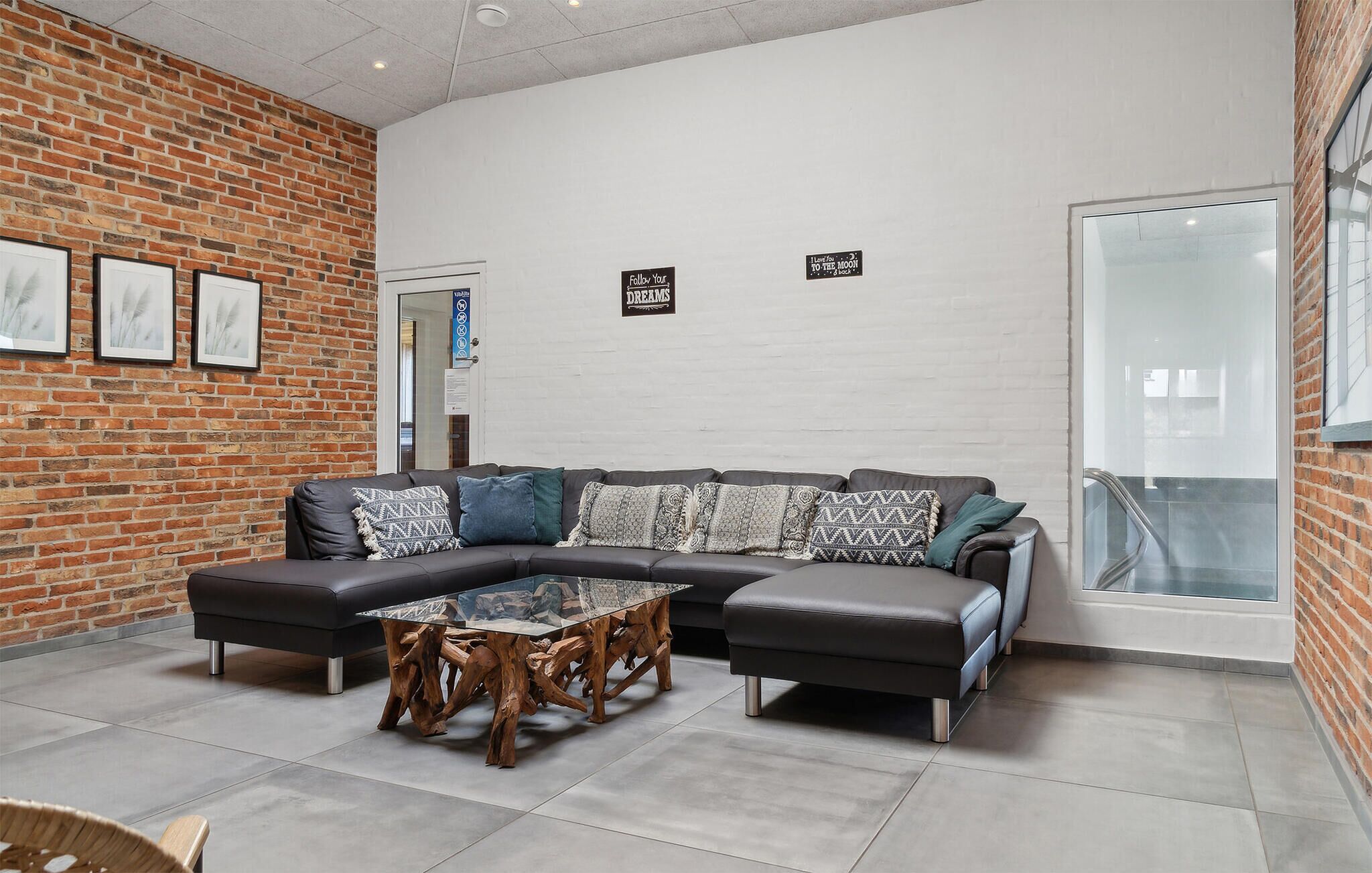 Ein modernes Wohnzimmer mit Backsteinwand, einem Ecksofa, einem Couchtisch mit Glasplatte und einem großen Fenster.