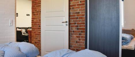 A bedroom with a brick wall, a white door, and a bed with blue bedding.