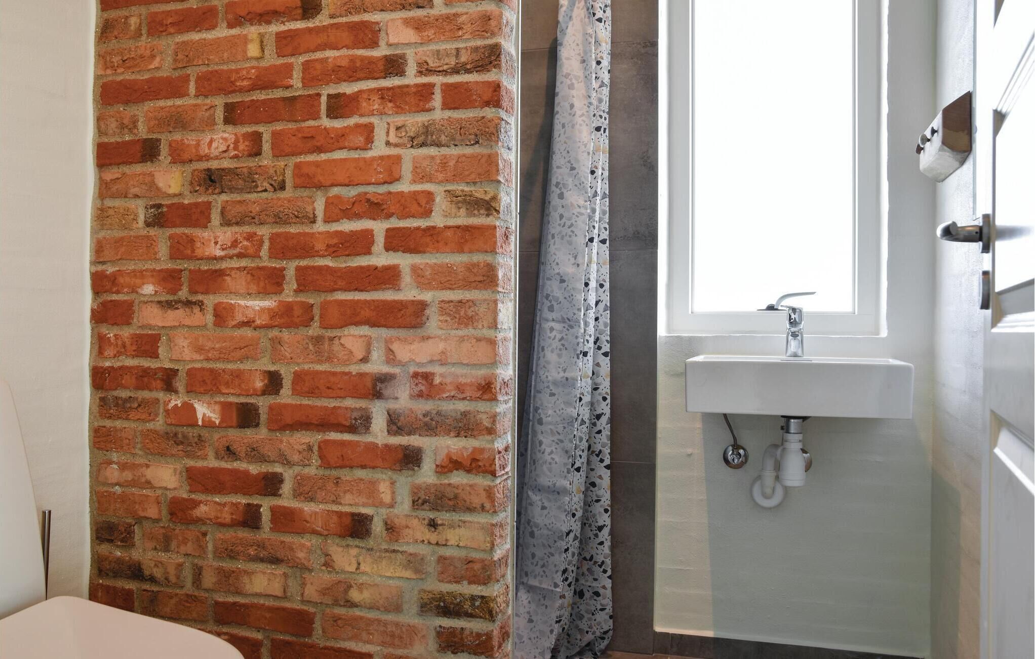 Une salle de bain avec un mur en briques, un lavabo blanc et une porte de douche en verre dépoli.