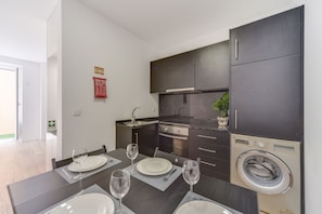 Une cuisine moderne avec des meubles de couleur sombre, un four encastré et un lave-linge.