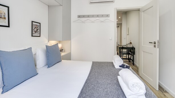 Ein Hotelzimmer mit Bett, Kissen, Nachttisch, Handtuch und Schreibtisch mit Stuhl.