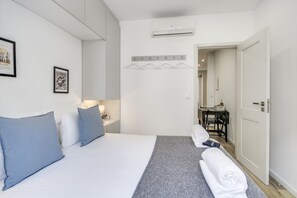A hotel room with a bed, pillows, a bedside table, a towel, and a desk with a chair. - Alcantara 65 Riverside (Lisbon)