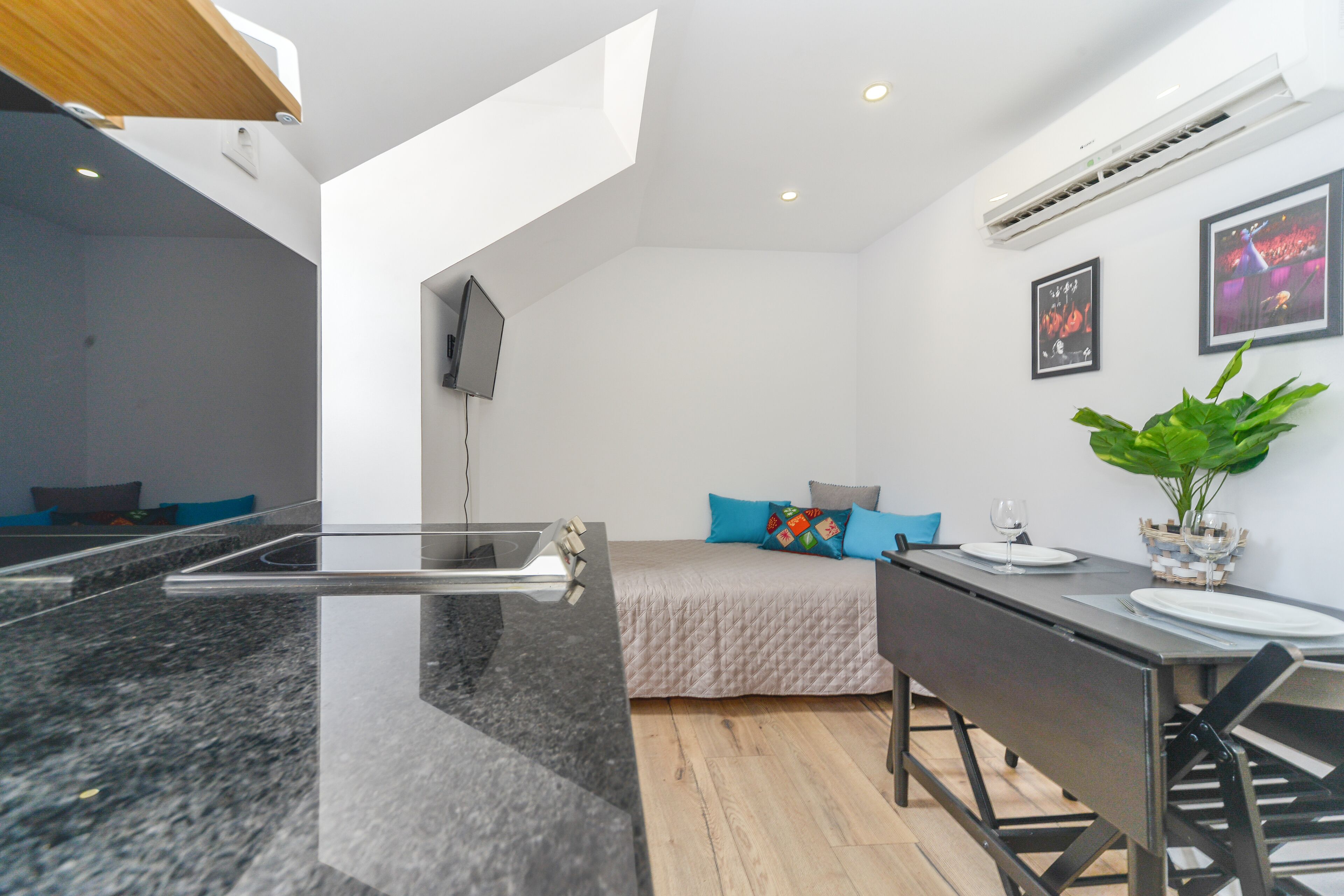 Eine moderne Küche mit einer Granit-Arbeitsplatte, ein Essbereich mit Tisch und Stühlen, ein Bett mit bunten Kissen und ein großes Fenster, das für natürliches Licht sorgt.