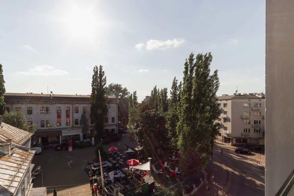 A courtyard with a market, buildings with balconies, and trees.