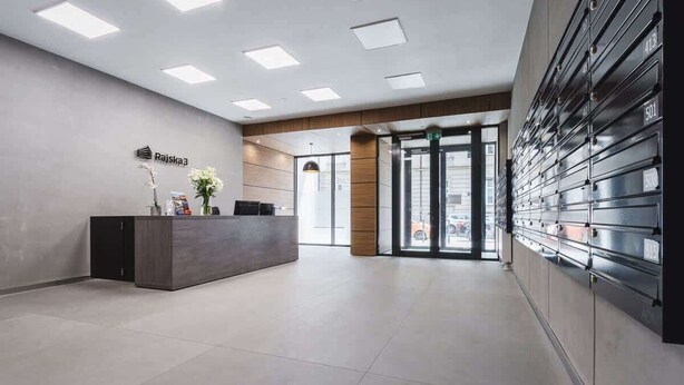 A modern reception area with a reception desk, a wall-mounted storage unit, and a glass door entrance. - Cracow | Rajska 3 | Modern Studio | Air conditioning (Kraków)