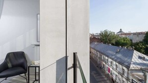 A balcony with a view of a street and buildings, a black chair, and a small table. - Cracow | Rajska 3 | Modern Studio | Air conditioning (Kraków)