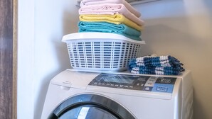 Un lave-linge à chargement frontal, avec un panier à linge et des serviettes empilés sur le dessus.
