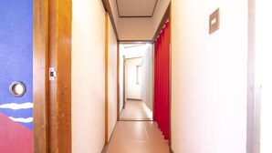Un couloir étroit, avec une porte en bois sur la gauche, un rideau rouge sur la droite et un interrupteur sur le mur.