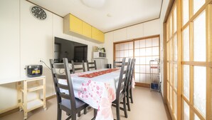 Un coin repas avec une table dressée pour quatre personnes, des chaises en bois, une horloge au mur et une porte coulissante donnant sur une vue agréable.