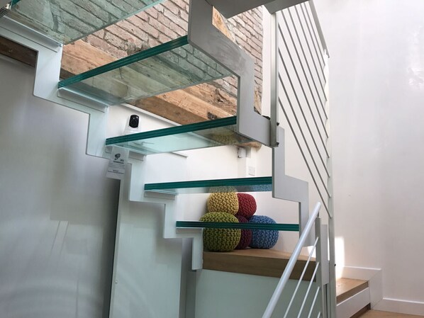 A modern staircase with glass railings and a wooden finish, leading to a landing with colorful knitted balls.