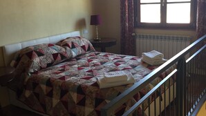Ein Schlafzimmer mit Bett, Nachttisch, Fenster mit Vorhängen und Heizkörper.