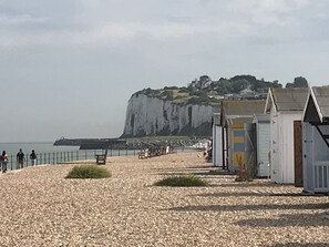 Une plage de galets avec une falaise en arrière-plan, une clôture et une rangée de petits bâtiments.