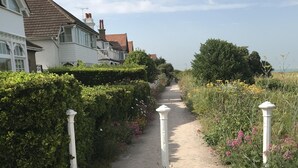 A gravel path flanked by hedges and white posts, leading to a residential area with houses. - 100 meters from the beach, Charming coastal period house. (Kingsdown Deal)