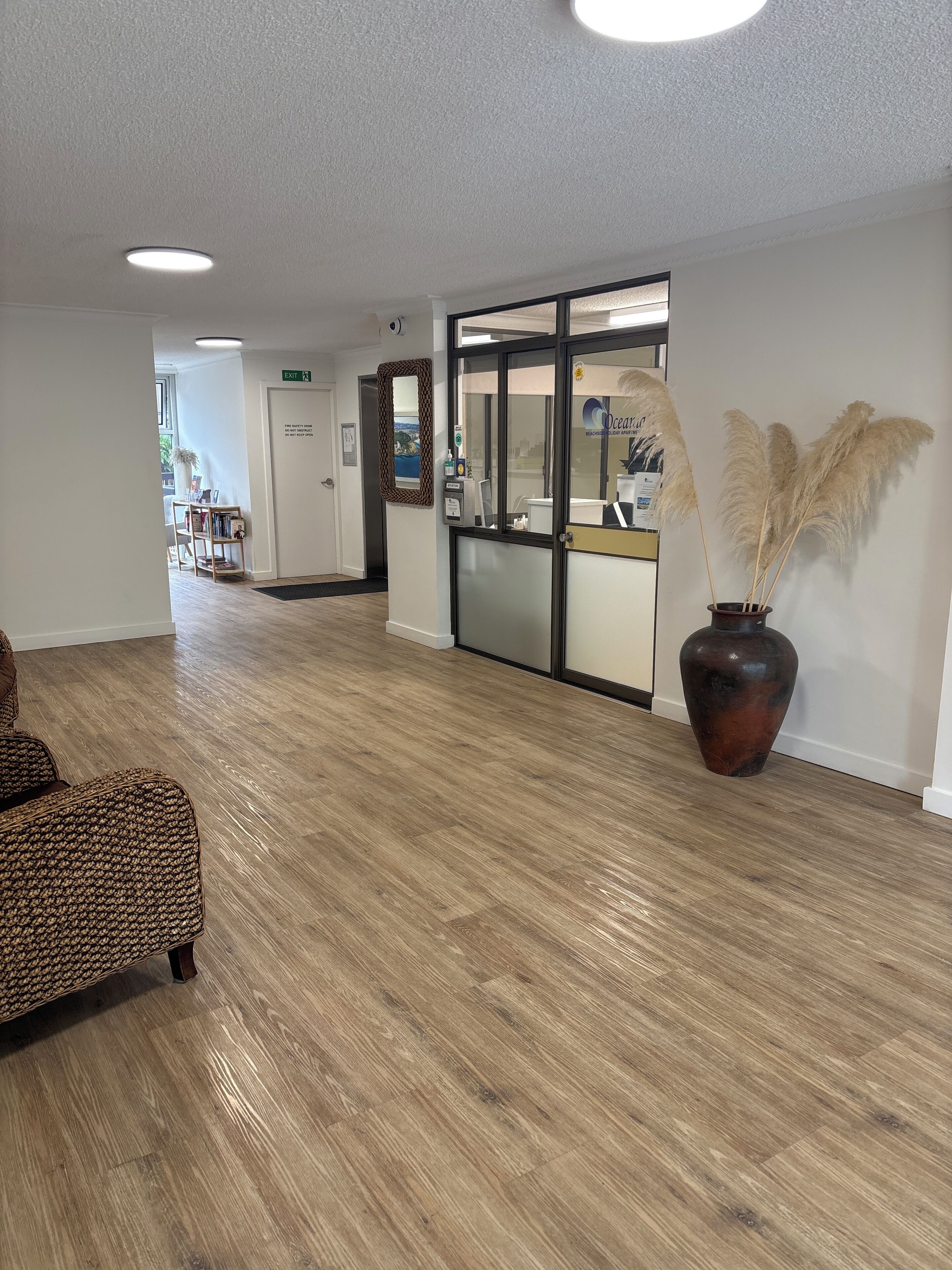 Un hall d’entrée spacieux, doté d’un plancher en bois, d’un comptoir de réception et d’un grand vase contenant des plumes d’herbe des pampas.