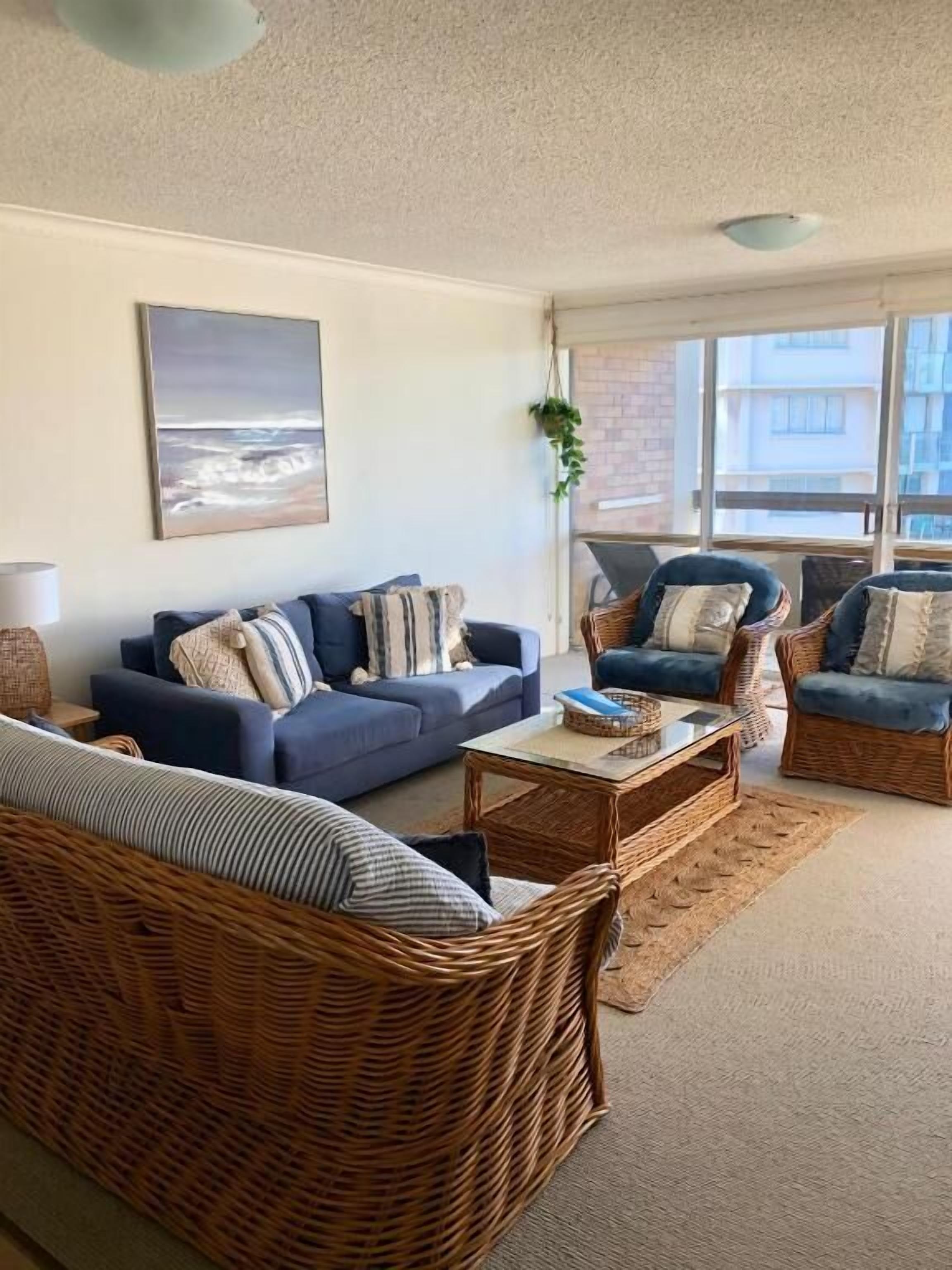 A living room with a sofa, armchairs, and a coffee table. There is a painting on the wall and a window providing natural light.