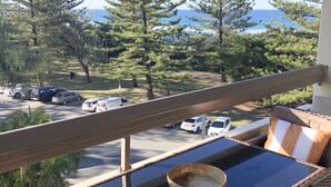 Ein Balkon mit Korbmöbeln, Blick auf einen Parkplatz und hohe Bäume.