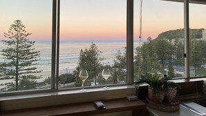 Ein Zimmer mit großem Fenster mit Blick auf Strand und Meer, ein Holztisch mit Fernbedienung und eine Zimmerpflanze.