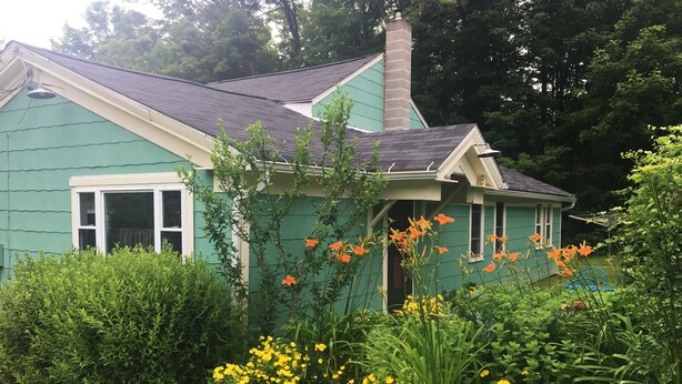 Una casa amb façana verda, una xemeneia i un jardí ple de flors grogues.