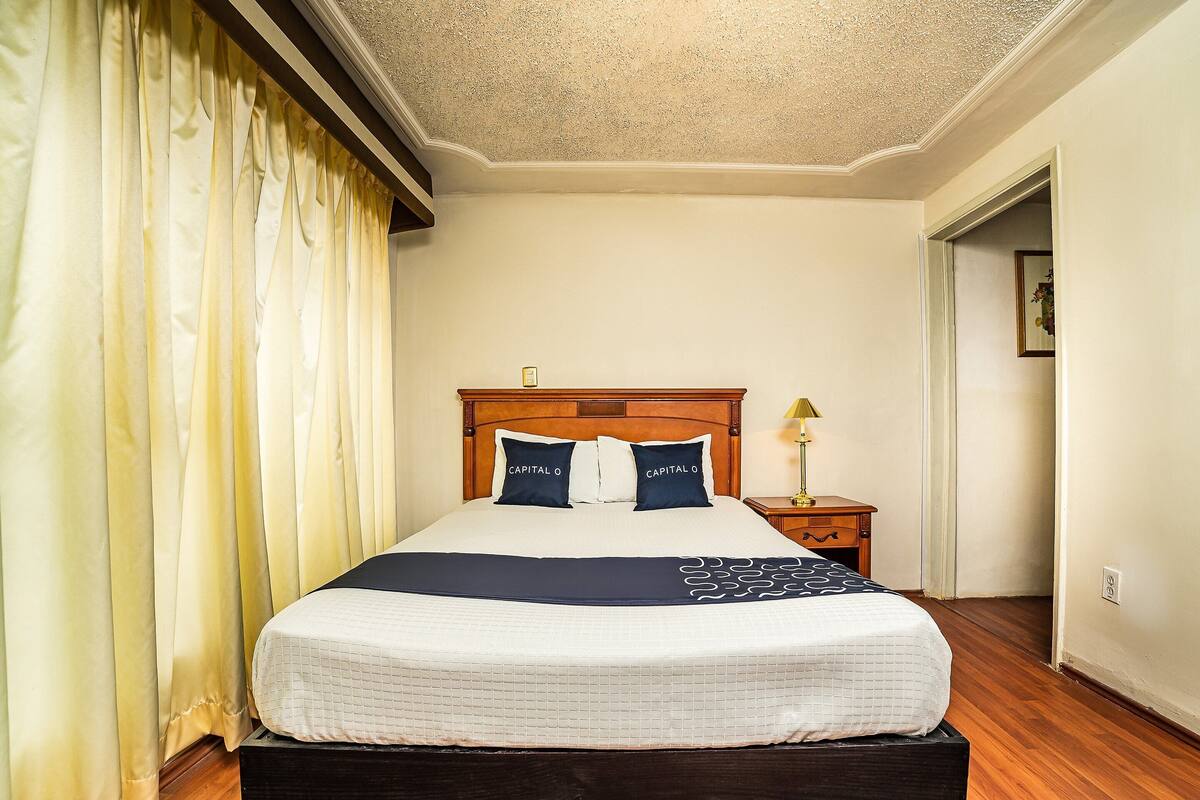 A neatly made bed with a wooden headboard, a bedside table with a lamp, and a door leading to another room.