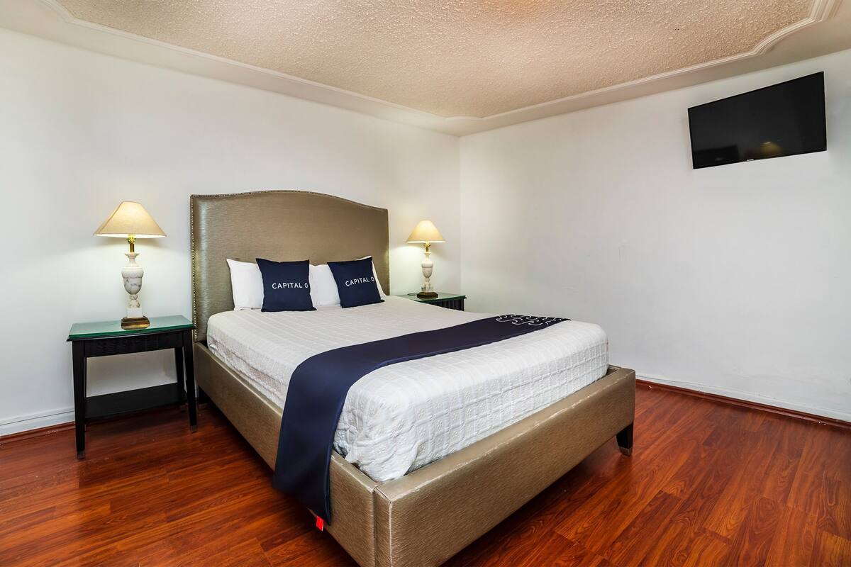 A neatly arranged bedroom with a large bed, two bedside tables with lamps, and a flat-screen TV mounted on the wall.