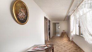 En hall med ett träbord, en inramad tavla och ett fönster med tunna, genomskinliga gardiner.