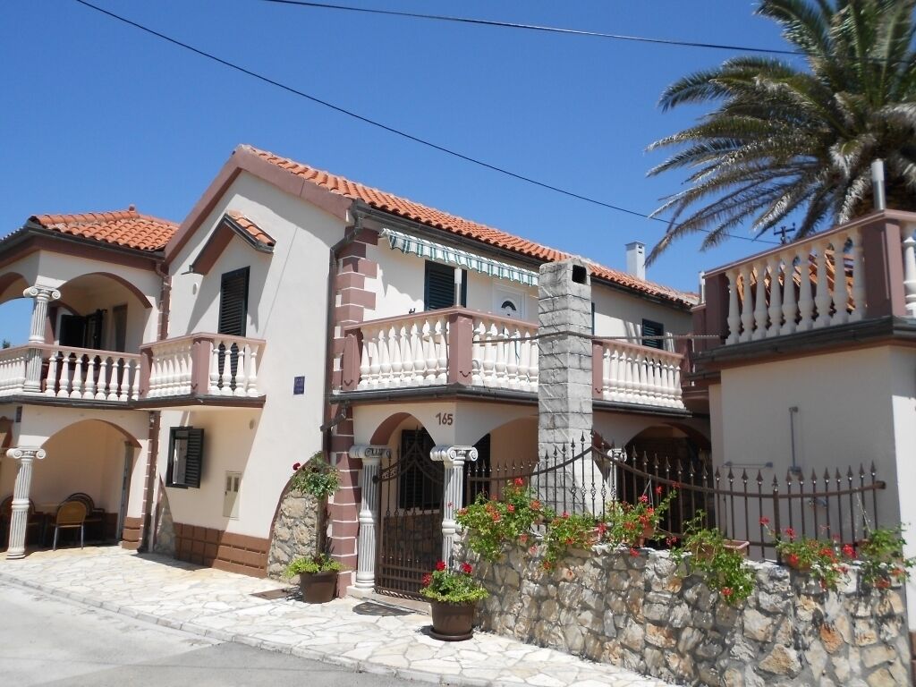 A two-story building with a tiled roof, stone walls, and a balcony with a railing.